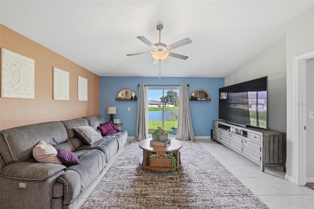 A living room features a gray sofa, a large television, and a view of a lake — 39745 HARVEST CREEK LANE, ZEPHYRHILLS, FL