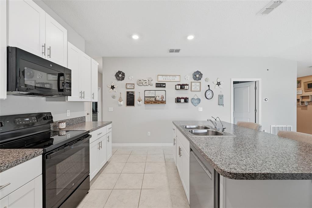 A kitchen features white cabinetry, granite countertops, a black oven, and a central island — 39745 HARVEST CREEK LANE, ZEPHYRHILLS, FL