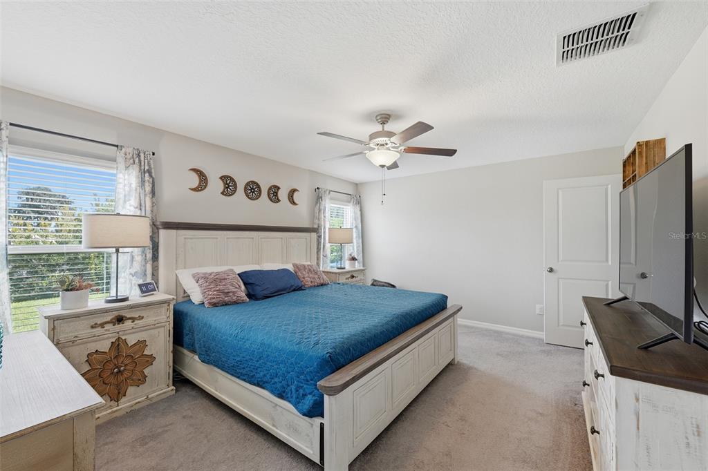 A bedroom features a bed with a blue quilt, white furniture, and moon phase wall decor — 39745 HARVEST CREEK LANE, ZEPHYRHILLS, FL