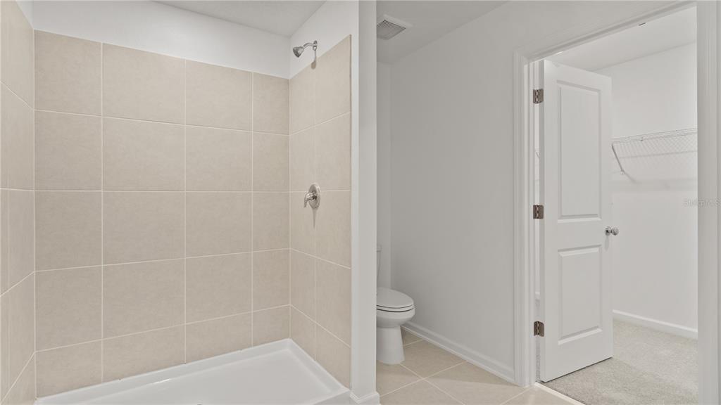 A tiled shower stall sits next to a toilet and an open walk-in closet door — 6260 BOTTICELLA BOULEVARD, WINTER HAVEN, FL