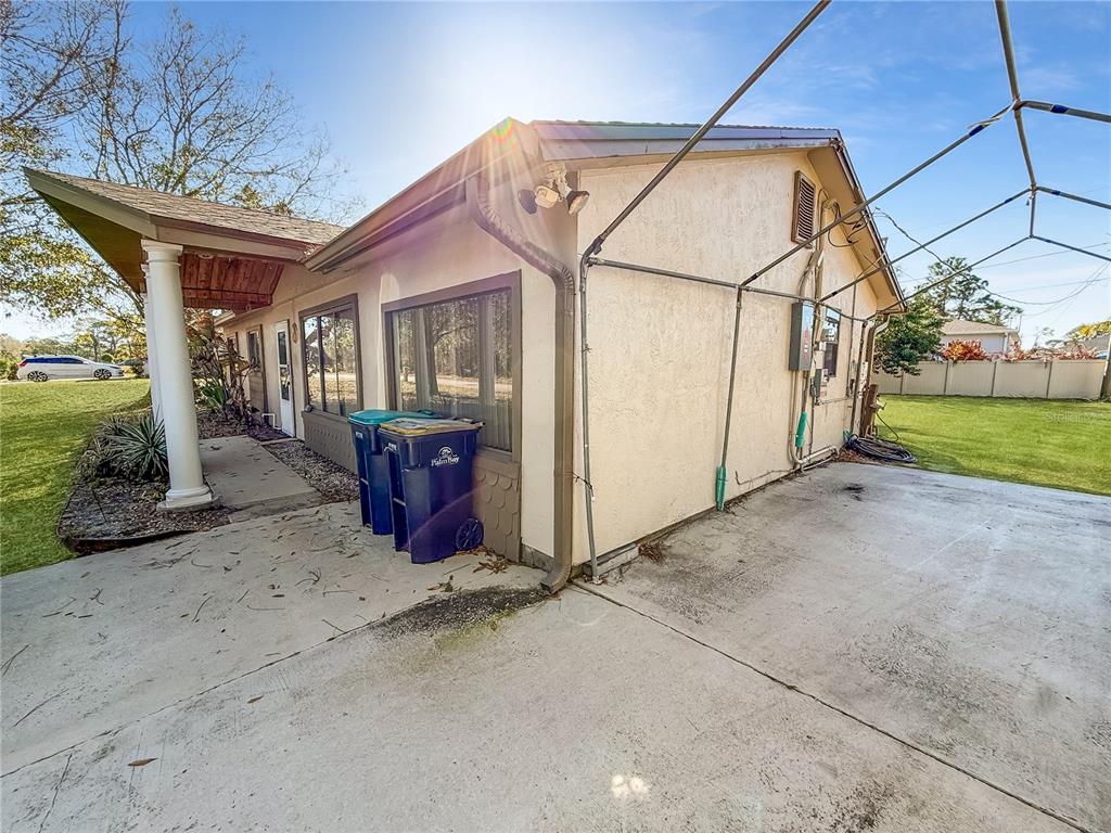 A side view of a house exterior with a concrete driveway and two blue trash bins — 1650 BURGUNDY STREET SE, PALM BAY, FL