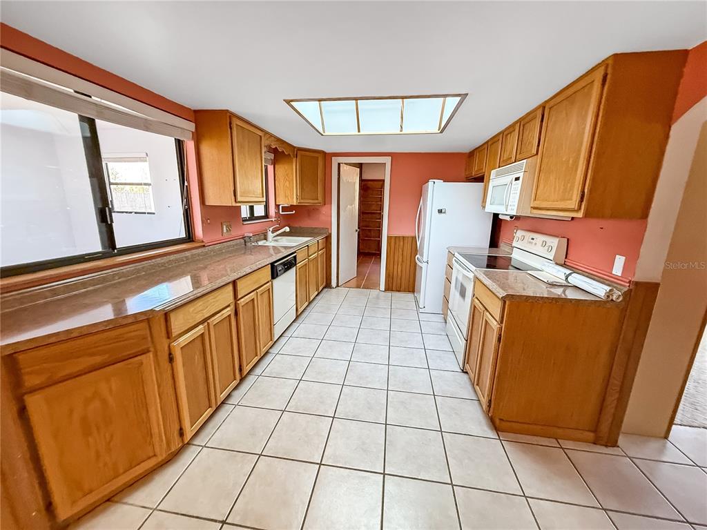 A kitchen with oak cabinets, laminate countertops, white appliances, and light-colored tile flooring — 1650 BURGUNDY STREET SE, PALM BAY, FL