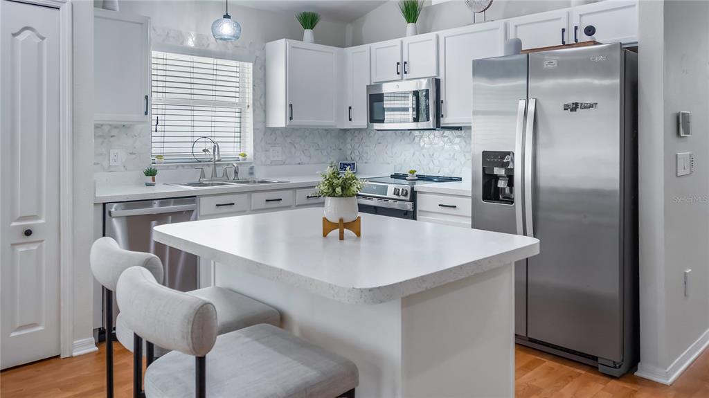 A kitchen features white cabinets, stainless steel appliances, a quartz island, and light wood flooring — 3931 ANDOVER CAY BOULEVARD, ORLANDO, FL
