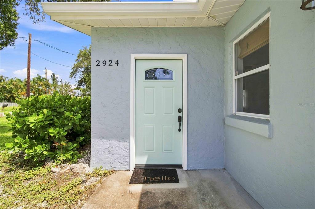 A light blue house exterior features a mint green front door and a welcome mat — 2924 HILLVIEW STREET, SARASOTA, FL