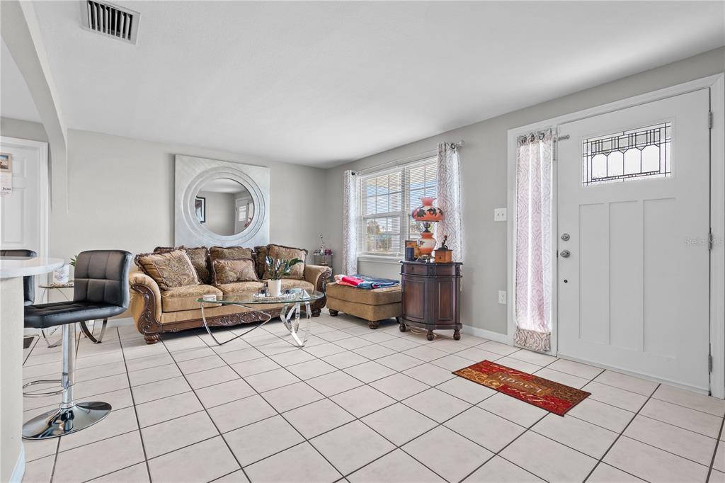 A living room features light tile flooring, a tan sofa, a round mirror, and a front door — 13323 NEPTUNE DRIVE, HUDSON, FL