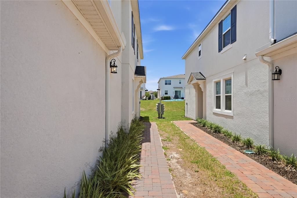 A narrow brick walkway sits between two white stucco townhomes with exterior wall lanterns — 1122 SEASIDE MIST TRAIL, KISSIMMEE, FL
