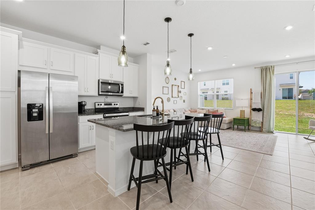 A kitchen with white cabinets, stainless steel appliances, and an island with three black chairs — 1122 SEASIDE MIST TRAIL, KISSIMMEE, FL