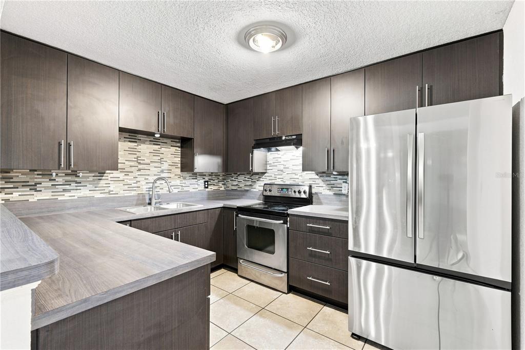 A kitchen features dark wood cabinets, stainless steel appliances, and a tiled backsplash — 3410 CALUMET DRIVE, ORLANDO, FL