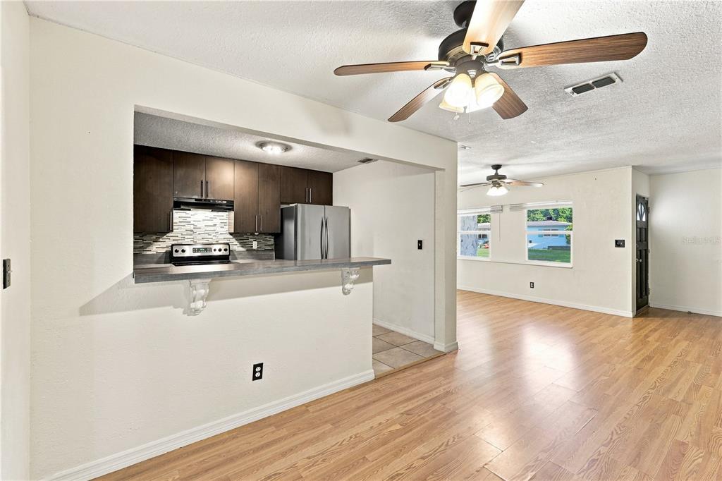 A kitchen with dark cabinets and a breakfast bar overlooks a living area with wood floors — 3410 CALUMET DRIVE, ORLANDO, FL