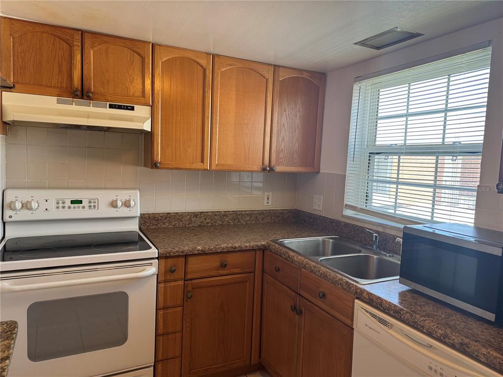 A kitchen features wood cabinets, a white stove, a double sink, and a window with blinds — 8542 10TH STREET N UNIT C, ST PETERSBURG, FL