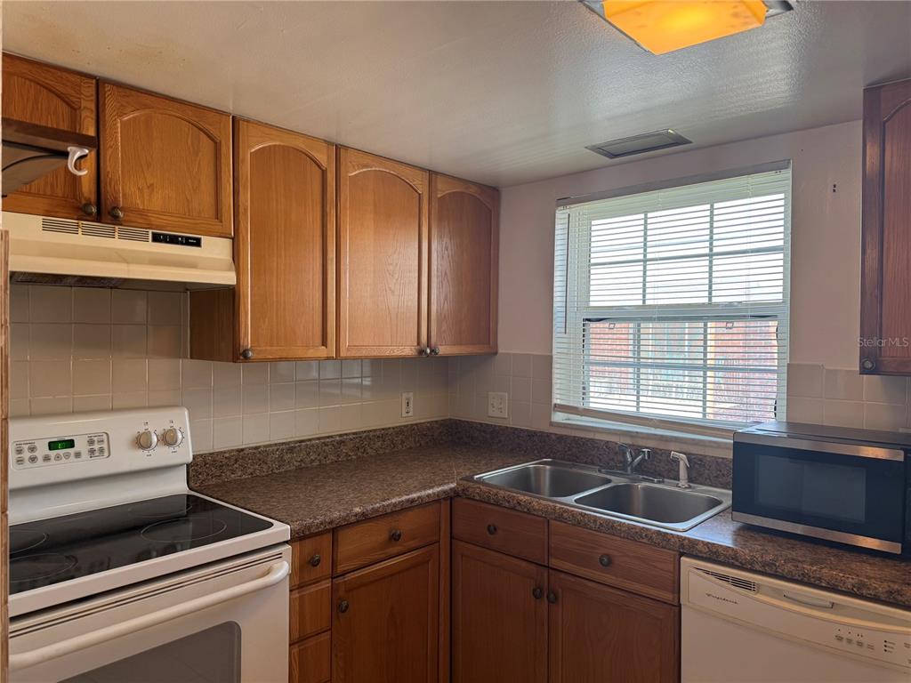 A kitchen features wood cabinets, laminate countertops, a white stove, and a double-basin sink — 8542 10TH STREET N UNIT C, ST PETERSBURG, FL