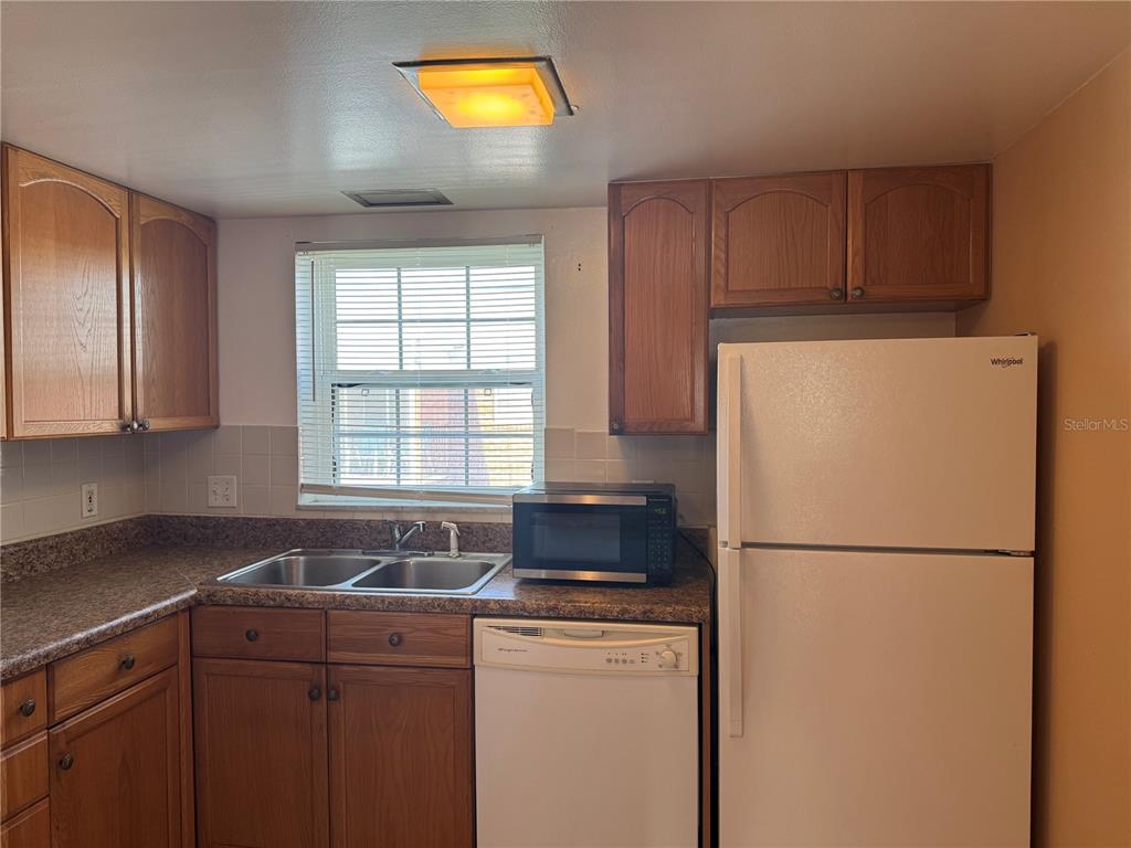 A kitchen features wood cabinets, a white refrigerator, a dishwasher, and a double-basin sink — 8542 10TH STREET N UNIT C, ST PETERSBURG, FL