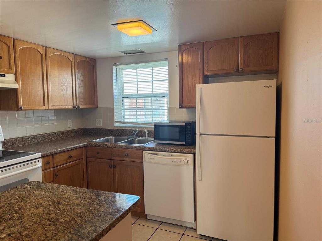 A kitchen features wood cabinets, a white refrigerator, a dishwasher, and a window above the sink — 8542 10TH STREET N UNIT C, ST PETERSBURG, FL
