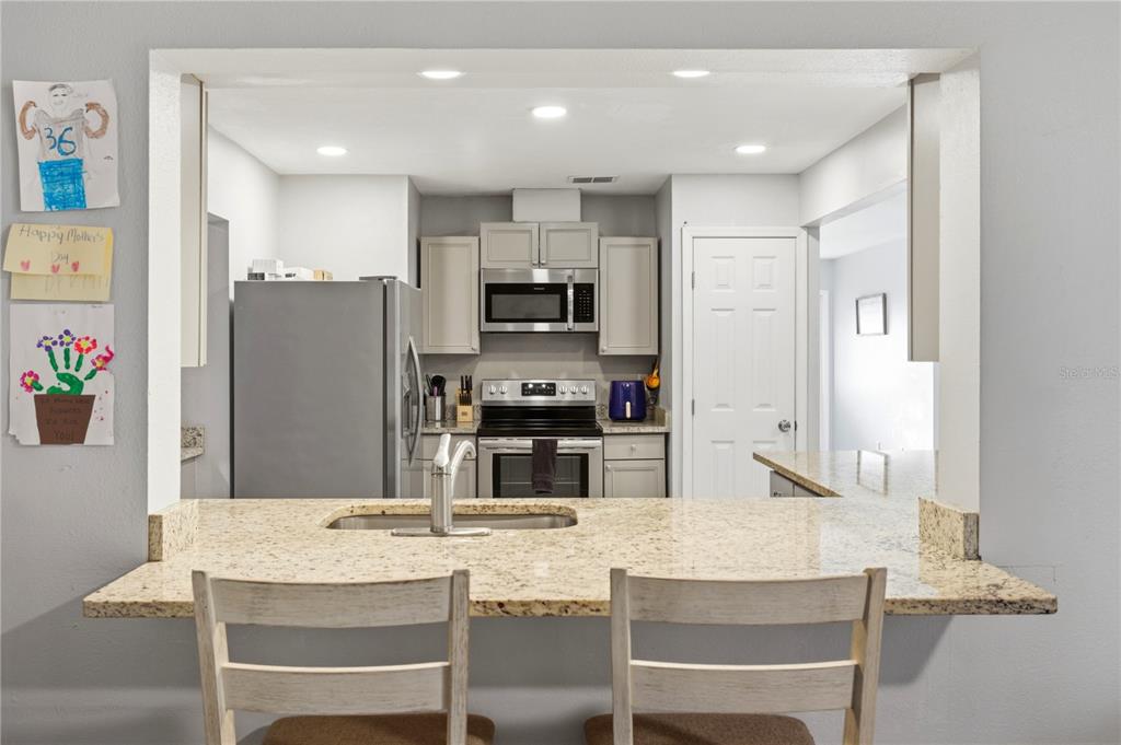 A kitchen features light gray cabinets, stainless steel appliances, and a granite-topped breakfast bar — 3634 LULLABY ROAD, NORTH PORT, FL