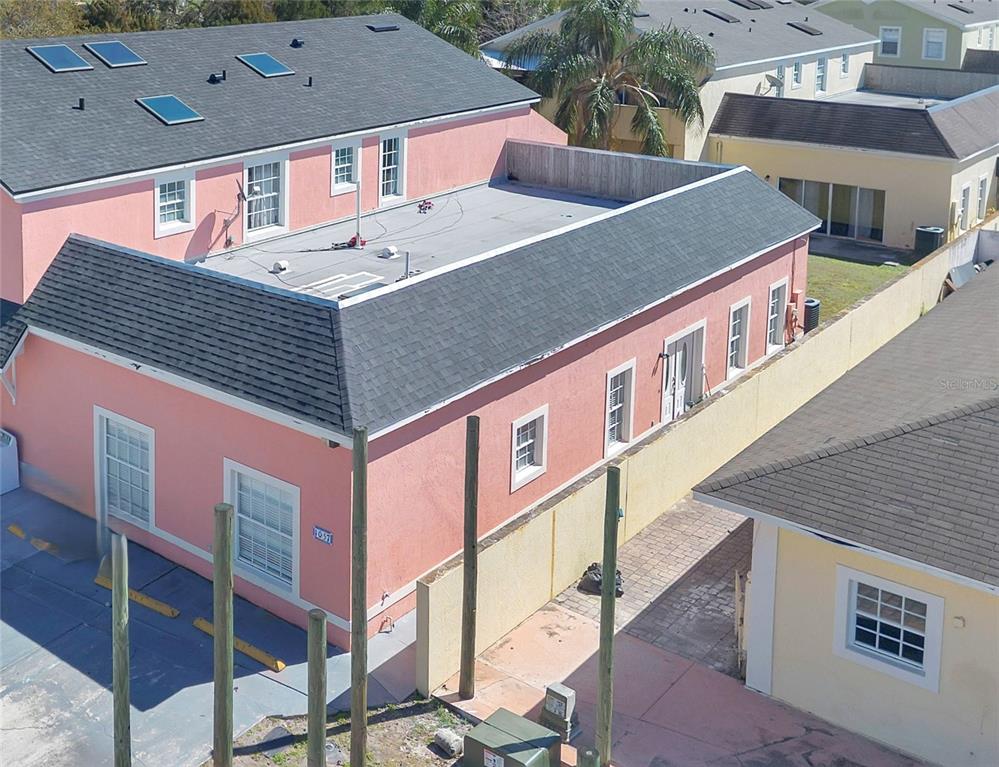An aerial view shows a pink building with a flat roof section and gray shingles — 1057 UNIVERSAL REST PLACE, KISSIMMEE, FL