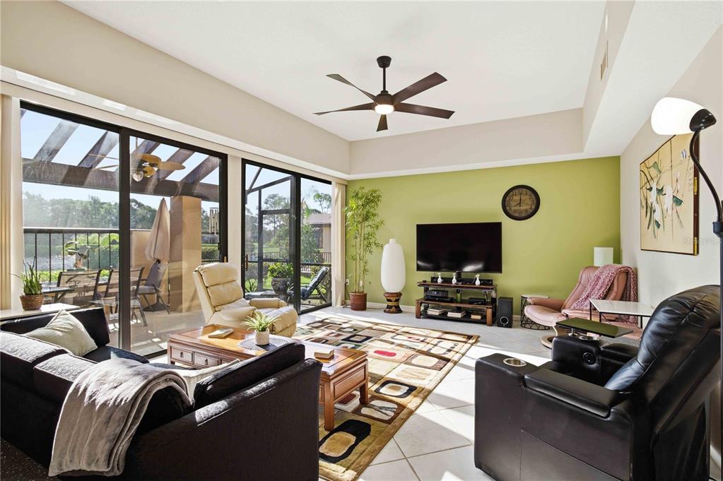A living room with a green accent wall, tile floors, a ceiling fan, and sliding doors — 5257 MYRTLE WOOD UNIT 29, SARASOTA, FL