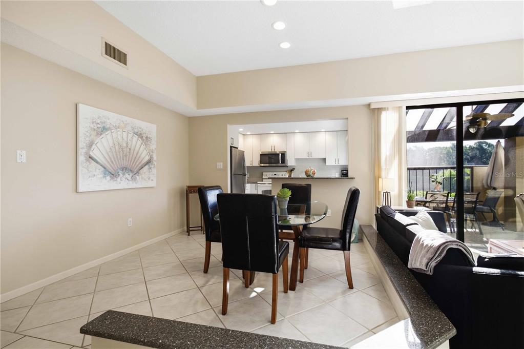 A dining area with a glass table and black chairs sits before an open kitchen — 5257 MYRTLE WOOD UNIT 29, SARASOTA, FL