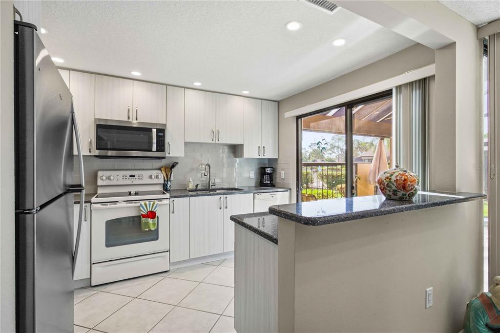 A kitchen with white cabinets, stainless steel appliances, a breakfast bar, and tile flooring — 5257 MYRTLE WOOD UNIT 29, SARASOTA, FL