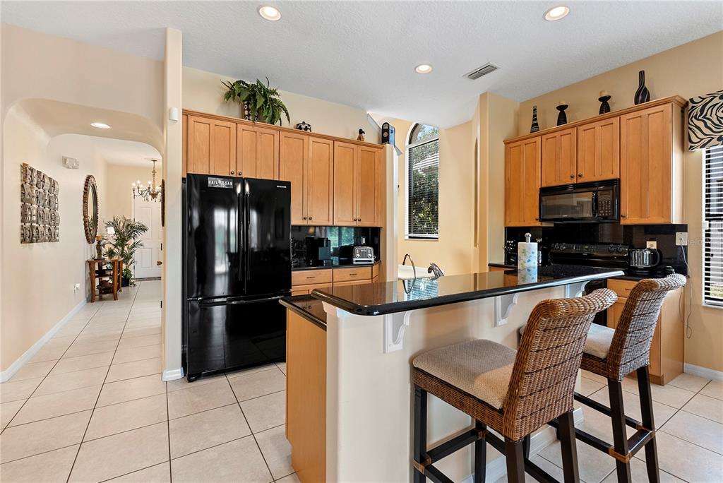 A kitchen features light wood cabinets, black appliances, a granite breakfast bar, and tile flooring — 358 LAKE DAVENPORT CIRCLE, DAVENPORT, FL