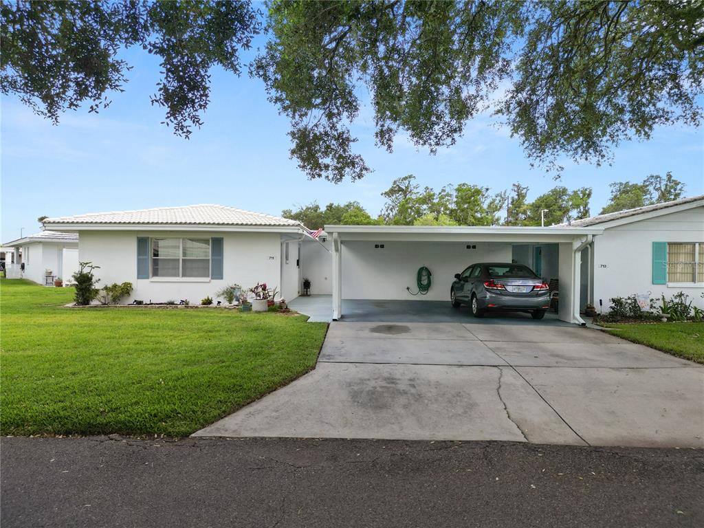 A white single-story house with a carport and a grassy lawn under a blue sky — 711 BARBER CIRCLE UNIT 711, LAKELAND, FL