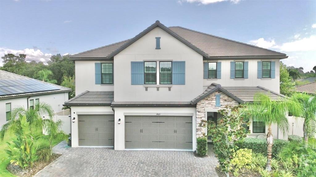 A two-story house with a stone facade, gray garage doors, and blue shutters — 19825 CYPRESS BRIDGE DRIVE, ODESSA, FL