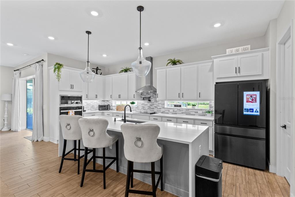 A modern kitchen features white cabinetry, a central island with bar stools, and stainless appliances — 13439 MCMILLAN DRIVE, ORLANDO, FL