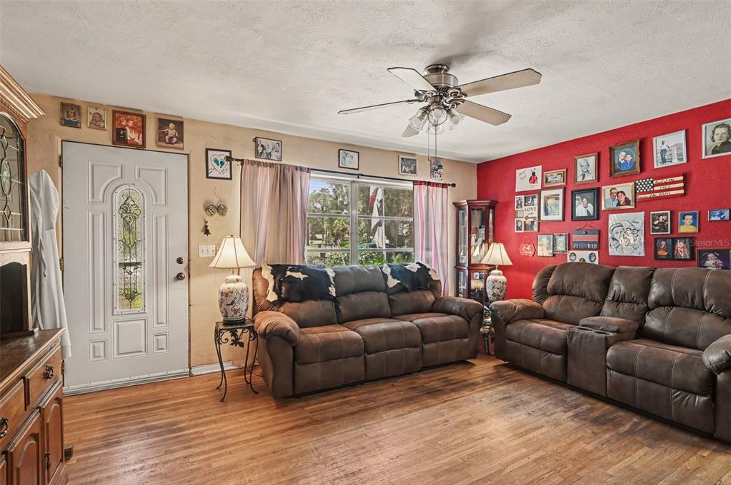 A living room features wood floors, a red accent wall with photos, and two brown sofas — 624 W FRENCH AVENUE, ORANGE CITY, FL