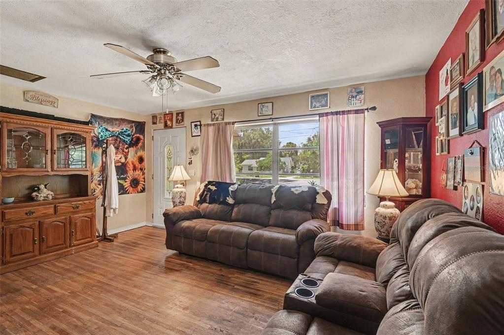 A living room features wood-look flooring, two brown reclining sofas, and a red accent wall — 624 W FRENCH AVENUE, ORANGE CITY, FL