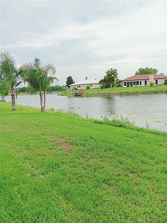 A grassy lawn overlooks a pond with houses visible on the opposite shore — 980 N GONDOLA DRIVE, VENICE, FL