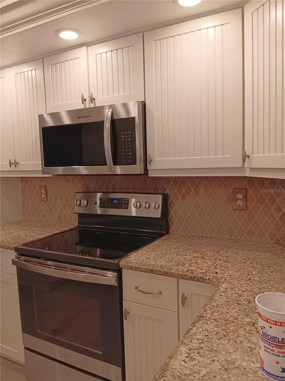 A kitchen features white beadboard cabinets, granite countertops, a stainless steel microwave, and a range — 980 N GONDOLA DRIVE, VENICE, FL