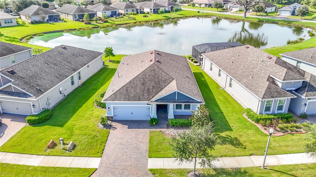 An aerial view shows suburban houses surrounding a central pond under a clear blue sky — 5252 CAPPLEMAN LOOP, BROOKSVILLE, FL