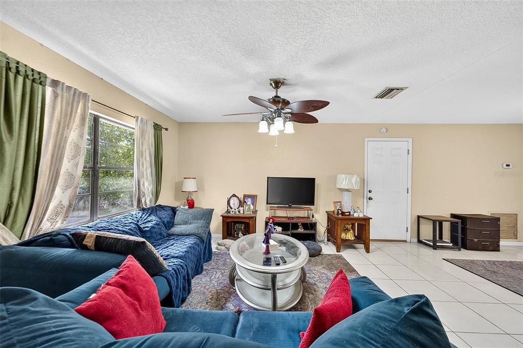 A living room features a blue sectional sofa, a glass coffee table, and tile flooring — 1917 CEDARBROOKE DRIVE, LUTZ, FL