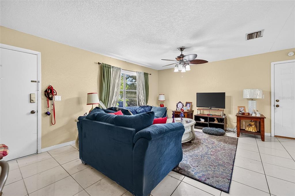 A living room features a blue sectional sofa, a television on a stand, and tile flooring — 1917 CEDARBROOKE DRIVE, LUTZ, FL
