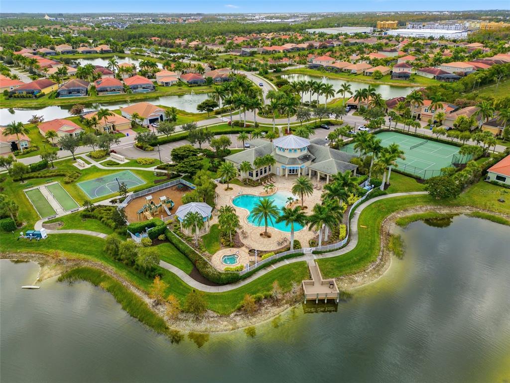 An aerial view of a community clubhouse featuring a pool, tennis courts, and a lake — 3987 ASHENTREE COURT, FORT MYERS, FL