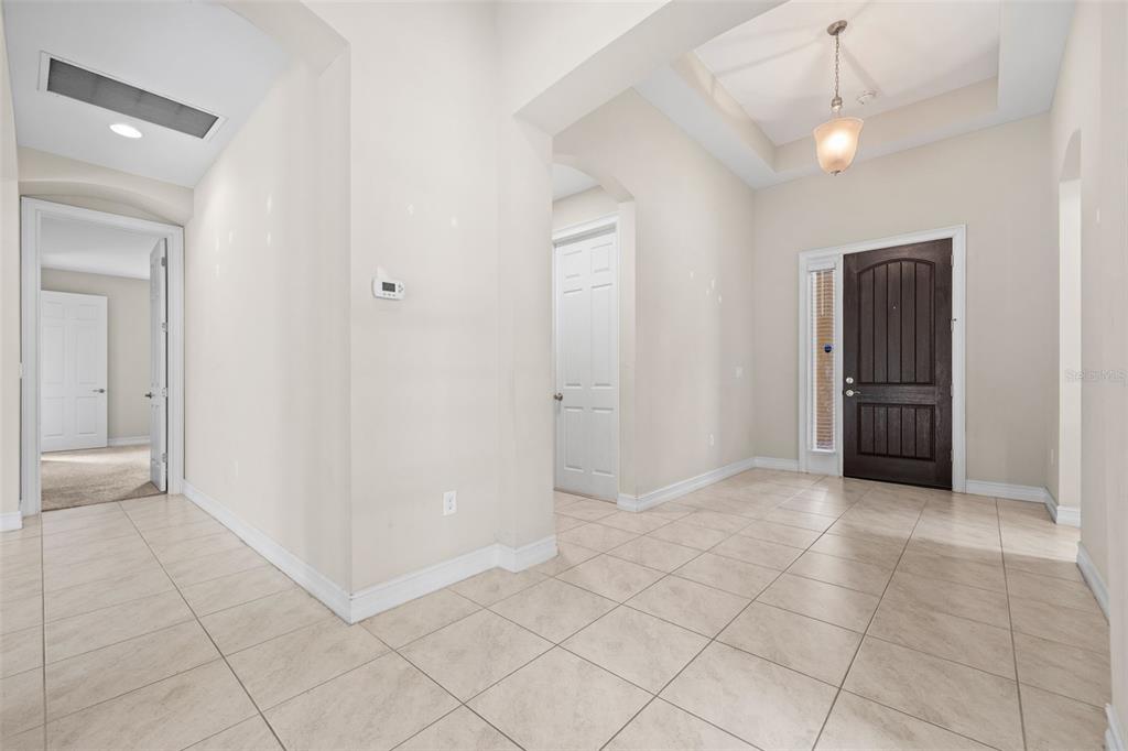 An entryway with beige tile flooring, a dark wood front door, and a tray ceiling — 3987 ASHENTREE COURT, FORT MYERS, FL