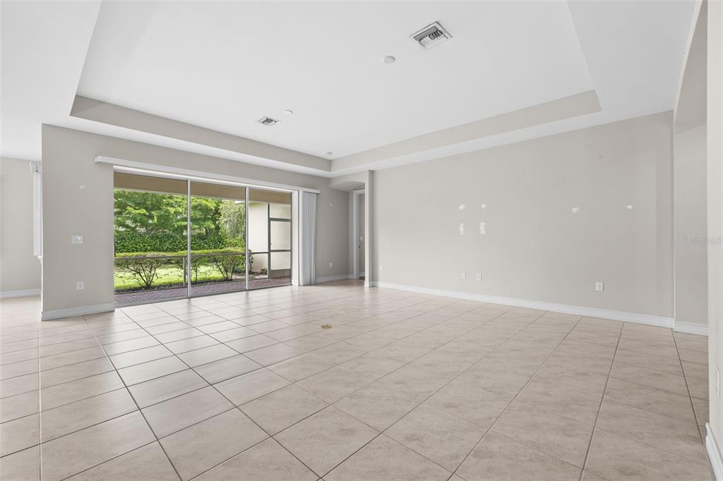 A spacious living room features light-colored tile flooring, a tray ceiling, and large sliding glass doors — 3987 ASHENTREE COURT, FORT MYERS, FL