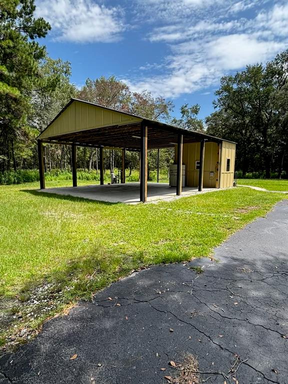 A metal-roofed open-air carport with an attached enclosed storage room stands on a grassy lot — 12125 NW 100TH STREET, OCALA, FL