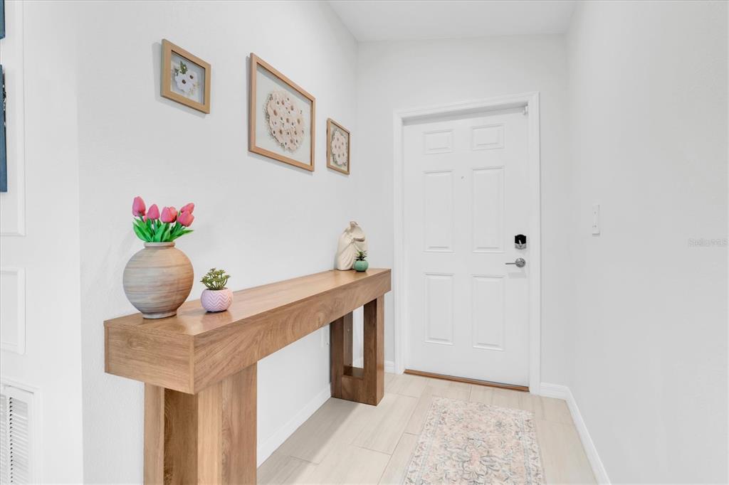A wooden console table sits in a white entryway with framed wall art and tile flooring — 10155 GENTLE RAIN DRIVE, LAND O LAKES, FL