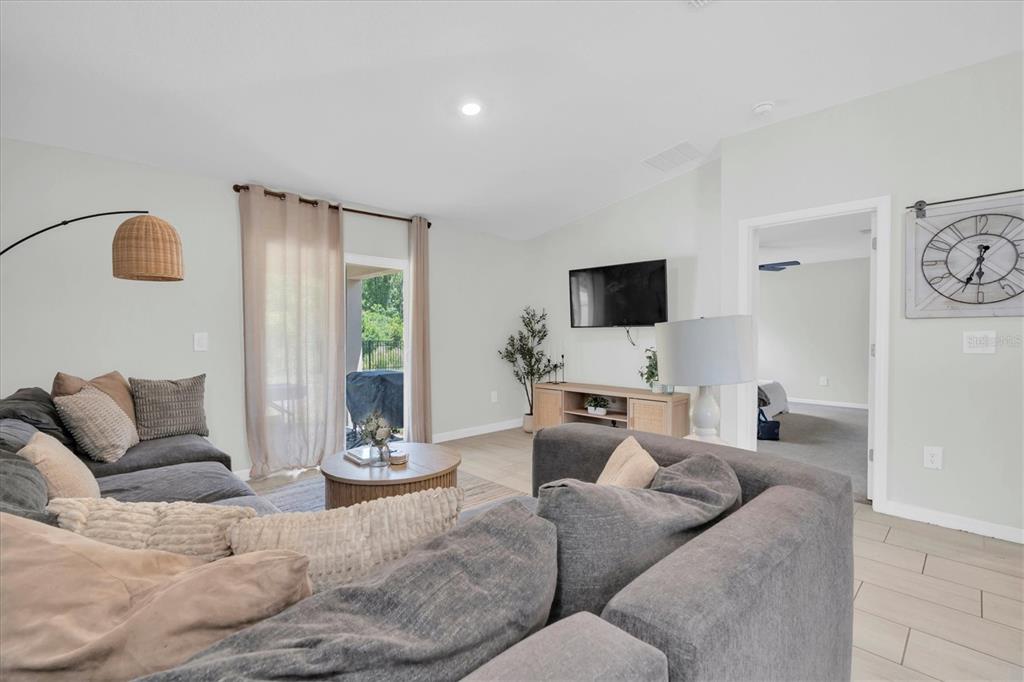 A living room features a gray sectional sofa, a wall-mounted television, and a sliding glass door — 10155 GENTLE RAIN DRIVE, LAND O LAKES, FL