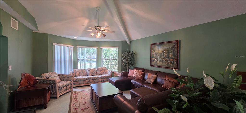 A living room features a vaulted ceiling, green walls, a sectional sofa, and bay windows — 10741 PINTO DRIVE, HUDSON, FL