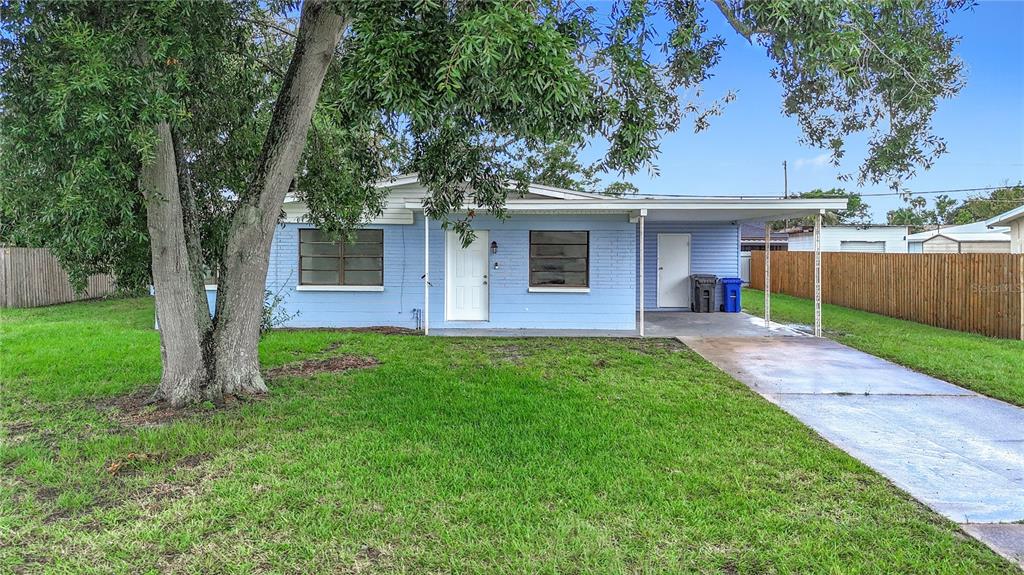 A light blue, single-story house with a front lawn, a large tree, and a carport — 6228 FLORIDA CIRCLE W, APOLLO BEACH, FL