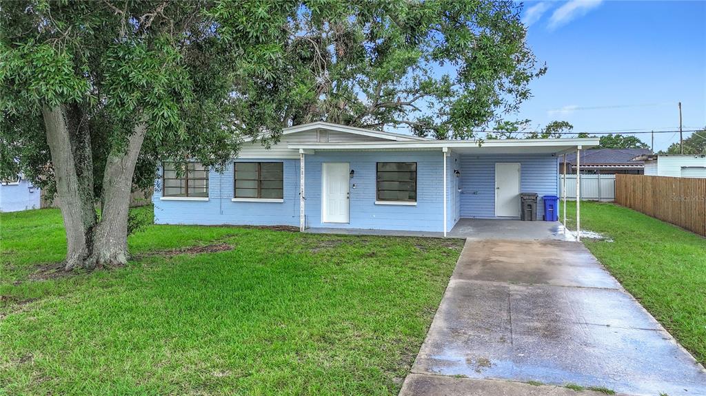 A light blue single-story house with a concrete driveway, carport, and a large front tree — 6228 FLORIDA CIRCLE W, APOLLO BEACH, FL
