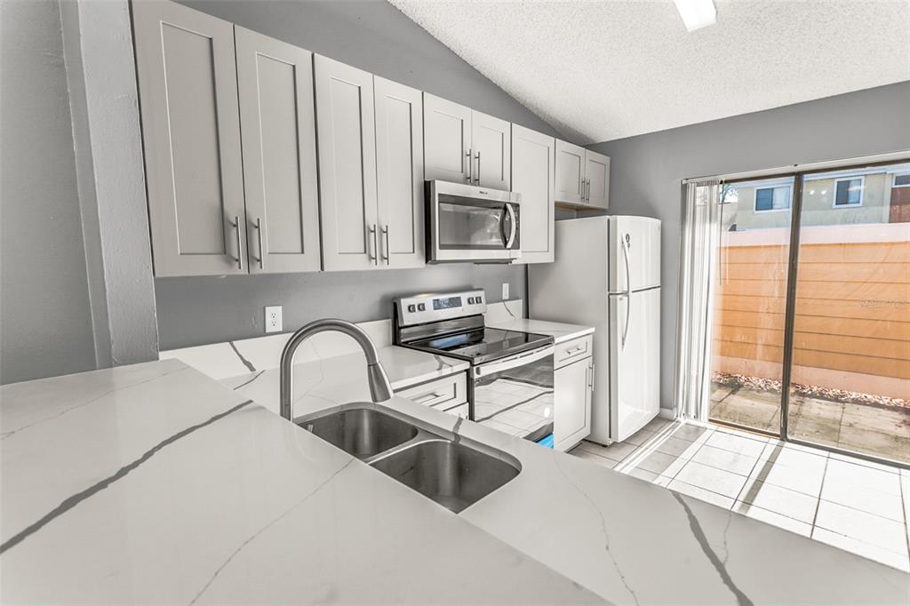 A kitchen features gray cabinets, white marble-look countertops, stainless steel appliances, and a sliding glass door — 85 SILVER PARK CIRCLE, KISSIMMEE, FL