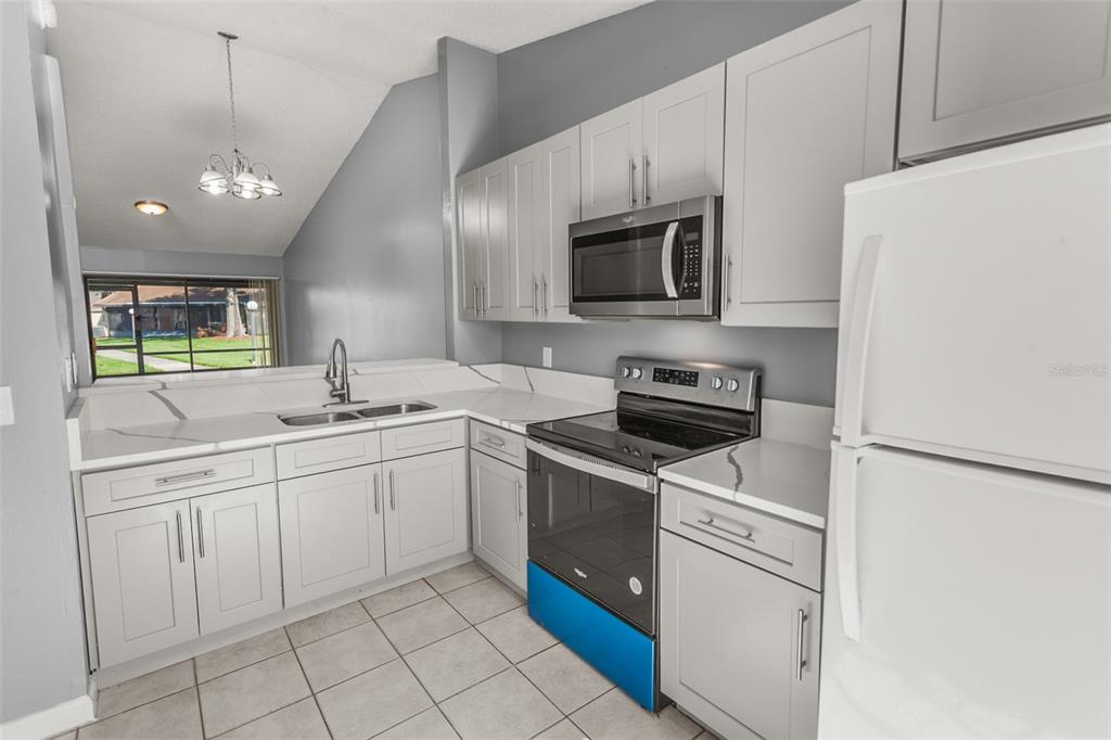 A kitchen features light gray cabinets, white countertops, stainless steel appliances, and tile flooring — 85 SILVER PARK CIRCLE, KISSIMMEE, FL