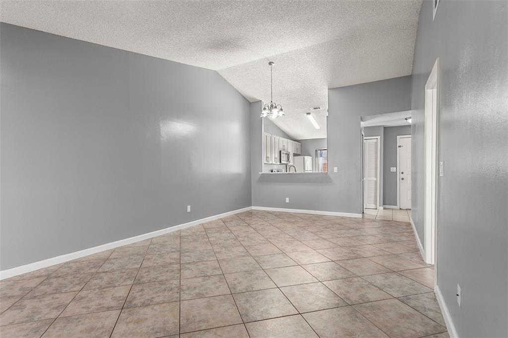 An empty room with gray walls, tile flooring, and a pass-through opening to the kitchen — 85 SILVER PARK CIRCLE, KISSIMMEE, FL