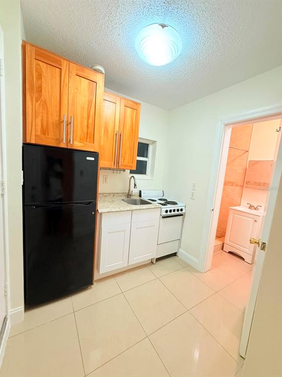 A small kitchen features light wood upper cabinets, white lower cabinets, and a black refrigerator — 2300 SW 24TH STREET, MIAMI, FL