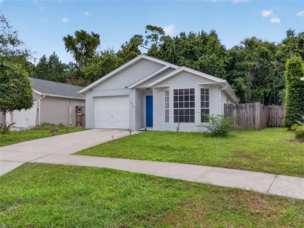 A single-story gray house with a white garage door, blue front door, and front lawn — 10225 CODY LANE, ORLANDO, FL