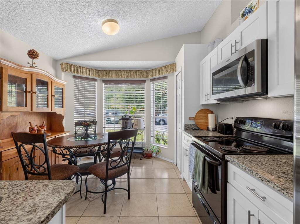 A kitchen with white cabinets, granite countertops, a black stove, and a dining nook area — 10225 CODY LANE, ORLANDO, FL