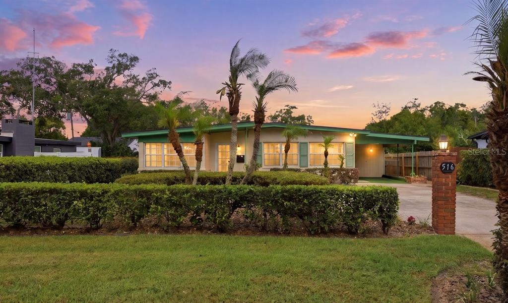 A single-story house with a carport and palm trees behind a manicured hedge at sunset — 516 S HIGHLAND AVENUE, WINTER GARDEN, FL