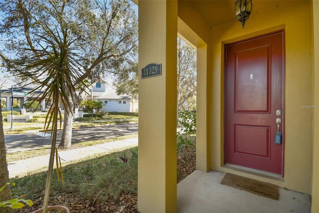 A red front door is set within a covered porch with a yellow pillar — 11329 RAVINIA PARK BOULEVARD, TAMPA, FL